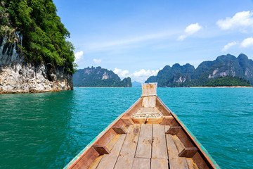 Wooden boat in green lake with limestone mountains and cliffs