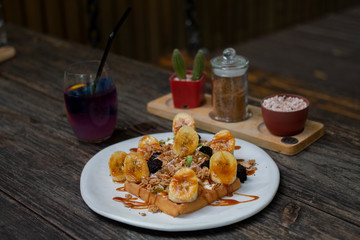 Delicious waffle pancake topping with banana and caramel syrup serves on white plate .