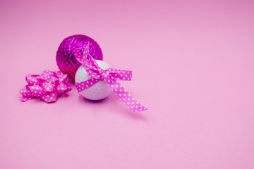 Golf ball with pink ribbon on pink background.