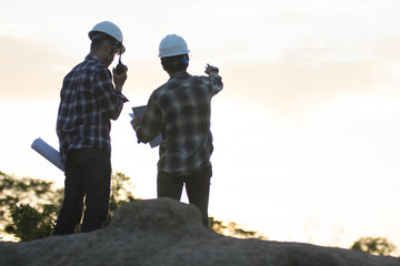 Blurry silhouette portrait of two engineers or architects pointing at the golden sky