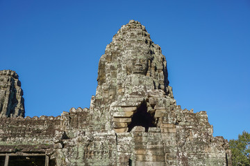 Naklejka premium Detail Mural faces in the stone of Bayon belong angkor thom nearly angkor wat is popularity of the site among tourists with blue sky in background. UNESCO World Heritage Site. Siem Reap, Cambodia