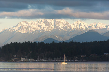 USA, Washington State, Puget Sound. Morning light on sailboat in Port Orchard Narrows. Snow-covered Olympic Mountains beyond Kitsap Peninsula - obrazy, fototapety, plakaty