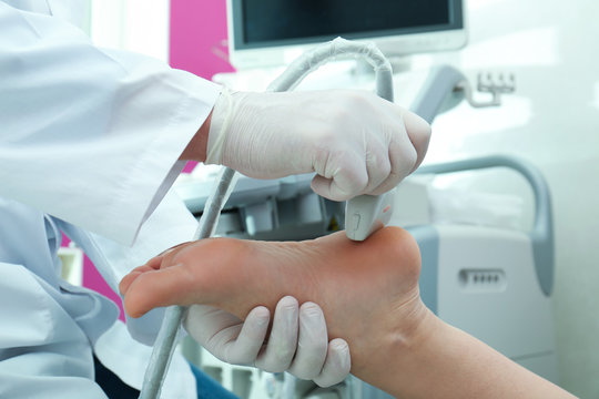 Doctor conducting ultrasound examination of patient's foot in clinic, closeup