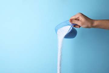 Woman pouring laundry detergent from measuring container against blue background, closeup. Space for text