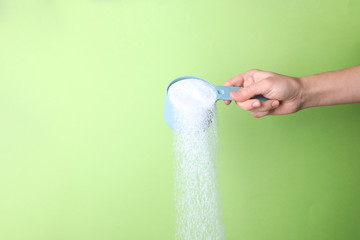 Woman pouring laundry detergent from measuring container against green background, closeup. Space...