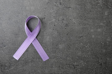 Purple ribbon on grey stone background, top view with space for text. Domestic violence awareness