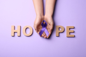 Woman with purple awareness ribbon and word HOPE made of wooden letters on violet background, top...