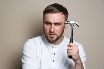 Young working man with hammer on beige background