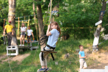 Little girl on zip line in adventure park. Summer camp