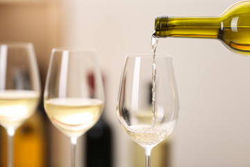 Pouring wine from bottle into glass on blurred background, space for text