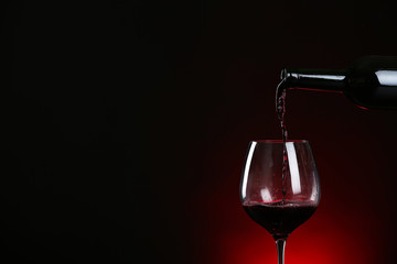 Fototapeta na wymiar Pouring wine from bottle into glass on dark background, space for text
