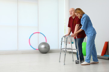 Caretaker helping elderly man with walking frame indoors