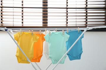 Different cute baby onesies hanging on clothes line indoors. Laundry day