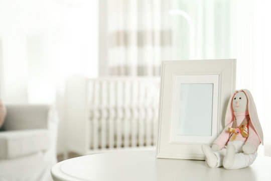 Photo frame and stuffed toy bunny on table in baby room interior. Space for text