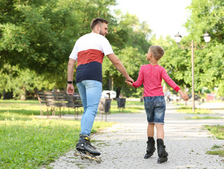 Obraz premium Father and son roller skating in summer park, back view