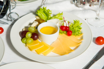 A restaurant dish of sliced cheese with honey and grapes on a table in a plate. Cold appetizer.