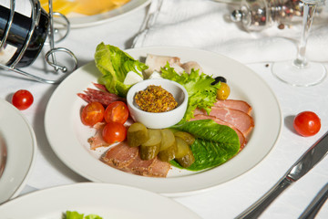Sliced sausage restaurant dish with pickles and cherry on a table in a plate. Cold appetizer.