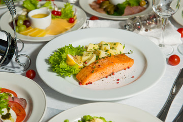A dish of salmon and boiled potatoes in a plate on the table. Hot restaurant dish.