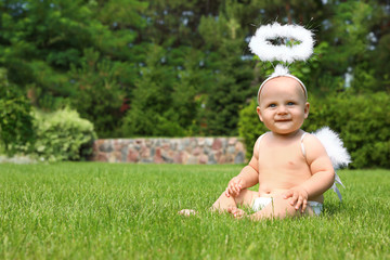 Little baby with angel wings and nimbus on green grass. Space for text