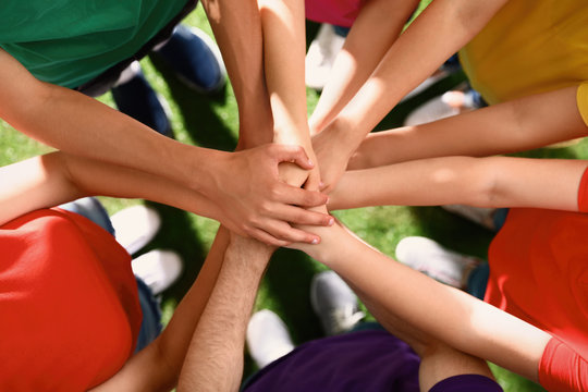 Group of volunteers joining hands together outdoors, top view
