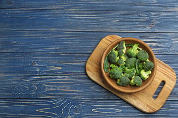 Bowl of fresh broccoli on blue wooden table, top view with space for text
