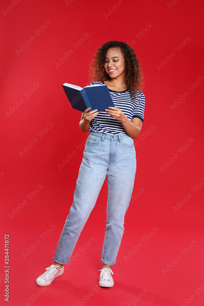 Wall mural beautiful african-american young woman reading book on red background