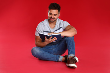 Handsome young man reading book on red background