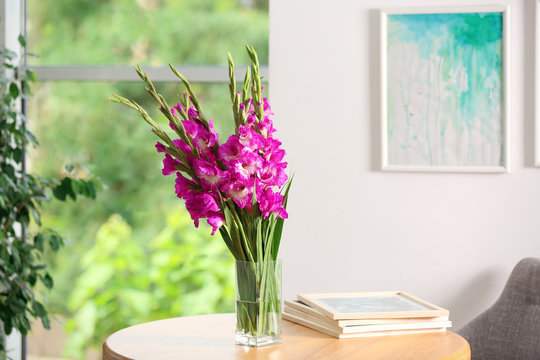 Vase with beautiful pink gladiolus flowers on wooden table in room, space for text