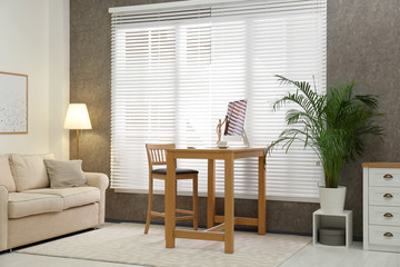 Comfortable workplace near window with blinds in room