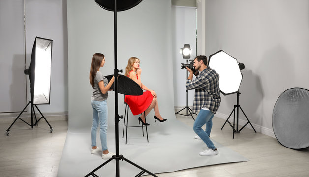 Professional photographer with assistant taking picture of young woman in modern studio
