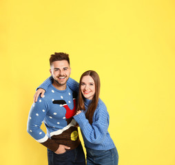Couple wearing Christmas sweaters on yellow background
