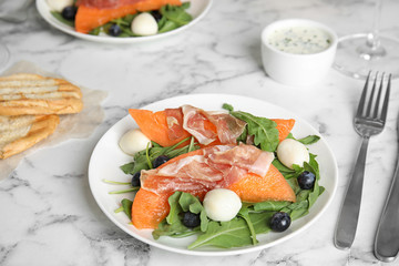 Fresh melon with prosciutto, mozzarella and arugula on marble table