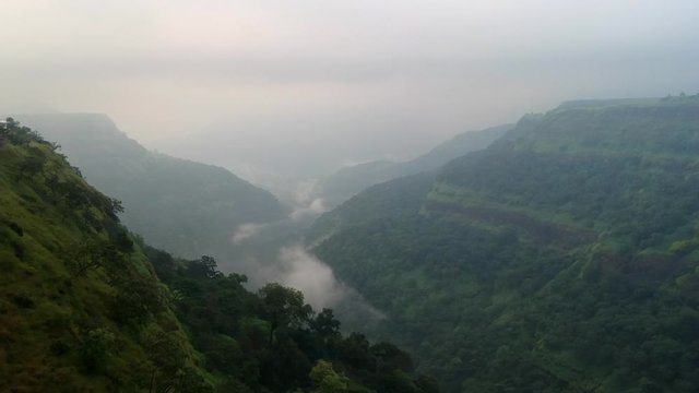 Slow panning drone shot of verdant misty canyon in India during rainy season