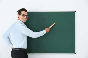 Young teacher with ruler near blank chalkboard in classroom. Space for text
