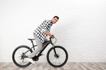 Fototapeta premium Handsome young man with modern bicycle near white brick wall indoors