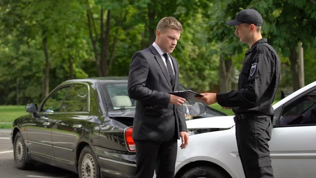 Upset businessman signing accident protocol with cop, auto collision, insurance