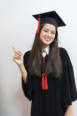 Asian graduate woman in cap gown on isolated white background wall.