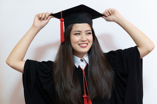 Asian graduate woman in cap gown on isolated white background wall.
