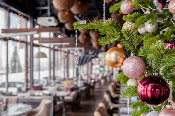 Closeup christmas new year decoration, fir spruce branches with shiny festive toys golden and pink balls on backgroun interior veranda modern restaurant, setting, serving banquet, chairs, tables