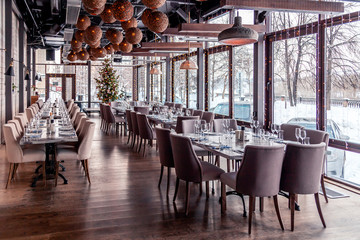 Christmas lights, decor, interior modern restaurant, panoramic windows, setting, serving banquet, gray textile chairs, serving tables, wine glass, plates, cutlery. Concept festive new year, winter