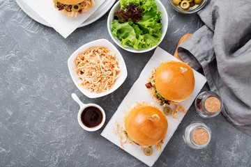 Pulled chicken sandwiches with barbeque sauce and lettuce on light blue or gray background.