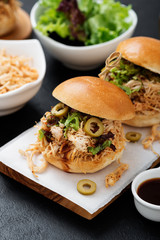 Pulled chicken sandwiches with barbeque sauce and lettuce on black background.