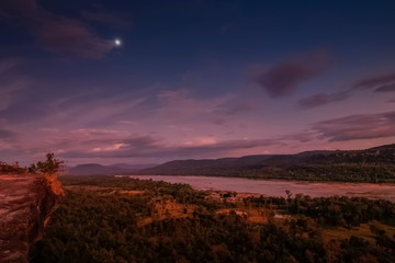 view of moon rising above Mekong river at night around with the hills and cloudy sky background, Pha Taem National Park, Ubon Ratchathani, Thailand.