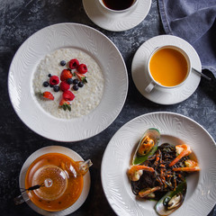 Menu at the cafe, Breakfast and lunch, Porridge with berries and pasta with seafood, Bulgur and black spaghetti with shrimps. Flatlay, Top view, Moody on black background, Darkstyle