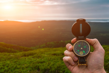 Travel, camping, orienteering and navigation concept - black magnetic compass close-up in a man s hand, blurred landscape background