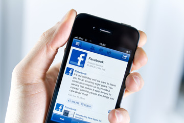 Kiev, Ukraine - February 08, 2012: Close-up shot of a man holding Apple iPhone with a Facebook profile page on a screen.