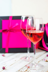 Two glasses of rose wine on white wooden table with pink gift boxes on background