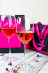 Two glasses of rose wine on white wooden table with pink gift boxes on background