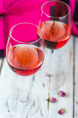 Two glasses of rose wine on white wooden table with pink gift boxes on background