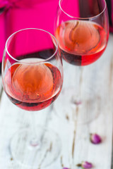 Two glasses of rose wine on white wooden table with pink gift boxes on background